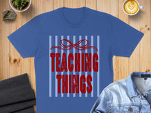 Load image into Gallery viewer, Blue t-shirt with red text "TEACHING THINGS" on striped background.