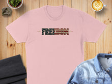 Load image into Gallery viewer, Pink t-shirt with "FREEDOM" in American flag text, on a wooden surface.