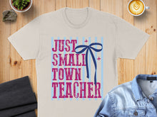 Load image into Gallery viewer, Beige t-shirt with "JUST SMALL TOWN TEACHER" text and blue bow graphic.
