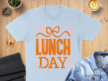 Load image into Gallery viewer, Light blue t-shirt with "Lunch Day" text and orange bow graphic.
