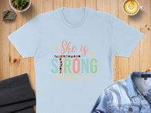 Load image into Gallery viewer, Light blue t-shirt with "She is STRONG" and "PROVERBS 31:25" text.
