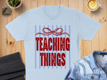 Load image into Gallery viewer, Light blue t-shirt with "TEACHING THINGS" in red text and a bow.