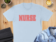 Load image into Gallery viewer, Light blue t-shirt with "NURSE" in red text, laid flat.