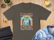 Load image into Gallery viewer, T-shirt with "Not all heroes wear capes, some wear scrubs" and a rainbow scrub top graphic.