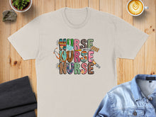 Load image into Gallery viewer, Beige t-shirt with "NURSE NURSE" in colorful, patterned letters and medical graphics.