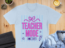 Load image into Gallery viewer, Light blue t-shirt with "Teacher Mode: On" text and pink bow graphic.