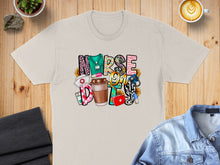 Load image into Gallery viewer, NURSE FUEL text with coffee, stethoscope, and sunflowers on a cream t-shirt.