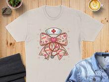 Load image into Gallery viewer, Cream t-shirt featuring a pink bow with hearts, stethoscope, and nurse's cap.