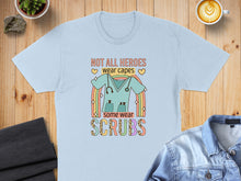Load image into Gallery viewer, Light blue t-shirt with "Not all heroes wear capes, some wear scrubs" and a scrub top graphic.