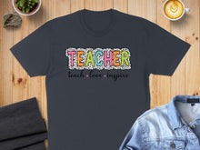 Load image into Gallery viewer, Dark t-shirt with "TEACHER" in colorful block letters and "teach love inspire" below.
