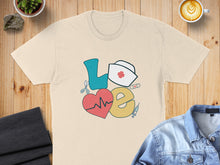 Load image into Gallery viewer, Cream t-shirt with "love" graphic featuring heart, stethoscope, and nurse hat.