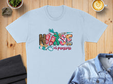 Load image into Gallery viewer, Light blue t-shirt with "Nurse in progress" graphic featuring medical tools and leopard print.