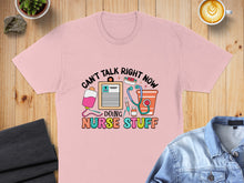 Load image into Gallery viewer, Pink t-shirt with "Can't Talk Right Now Doing Nurse Stuff" text and medical graphics.