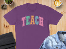 Load image into Gallery viewer, Purple t-shirt with "TEACH" in pastel block letters.