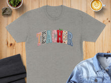 Load image into Gallery viewer, Grey t-shirt with "TEACHER" text in colorful, patterned letters.