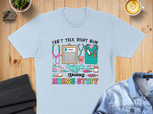 Load image into Gallery viewer, Light blue t-shirt with "Can't talk right now, doing nurse stuff" and medical icons.