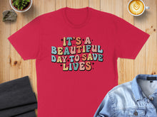 Load image into Gallery viewer, Red t-shirt with "It's a beautiful day to save lives" text in colorful retro font.