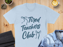 Load image into Gallery viewer, Light blue t-shirt with "Tired Teachers Club" graphic.