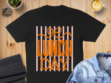 Load image into Gallery viewer, Black t-shirt with "LUNCH DAY" in orange letters against pink stripes.