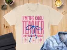 Load image into Gallery viewer, Cream t-shirt with "I'm the cool teacher they told you about" text and blue bow.