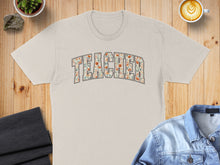 Load image into Gallery viewer, Beige t-shirt with "Teacher" text in floral pattern.