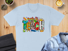 Load image into Gallery viewer, Light blue t-shirt with "made to TEACH" graphic featuring school supplies.