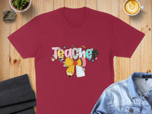 Load image into Gallery viewer, Maroon t-shirt with "Teacher" text in colorful, playful lettering and school-themed graphics.
