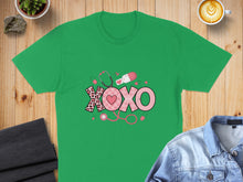 Load image into Gallery viewer, Green t-shirt with "XOXO" design featuring a stethoscope, pills, and heart pattern.