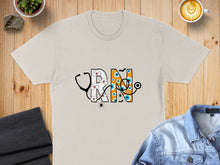 Load image into Gallery viewer, Cream t-shirt with "RN" text decorated with stethoscope, eyes, and spiders.
