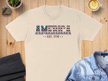 Load image into Gallery viewer, Cream t-shirt with "AMERICA EST. 1776" in distressed American flag lettering.