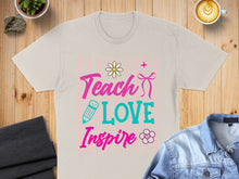 Load image into Gallery viewer, Light tan t-shirt with "Teach Love Inspire" text and floral graphics.