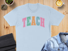 Load image into Gallery viewer, Light blue t-shirt with "TEACH" in colorful block letters.