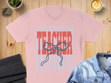 Load image into Gallery viewer, Pink t-shirt with "TEACHER" text and blue bow, laid flat with clothing.