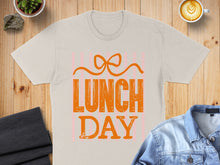 Load image into Gallery viewer, Beige t-shirt with "LUNCH DAY" text and orange bow graphic.