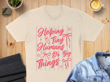 Load image into Gallery viewer, Cream t-shirt with pink text reading "Helping Tiny Humans Do Big Things".