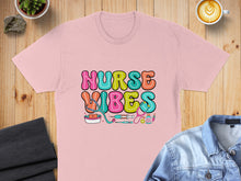 Load image into Gallery viewer, Pink t-shirt with colorful "Nurse Vibes" text and medical icons.