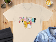 Load image into Gallery viewer, Cream t-shirt with "Teacher" text in colorful, playful lettering and school supplies.