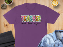 Load image into Gallery viewer, Purple t-shirt with "TEACHER" in colorful block letters and "teach love inspire" below.