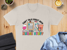 Load image into Gallery viewer, Beige t-shirt with colorful "CAN'T TALK RIGHT NOW DOING NURSE STUFF" graphic.