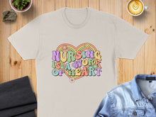 Load image into Gallery viewer, Beige t-shirt with "Nursing is a work of heart" rainbow text and flowers.