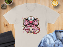 Load image into Gallery viewer, Cream t-shirt with a pink nurse's cap and stethoscope bowtie graphic.