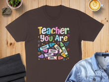 Load image into Gallery viewer, Brown t-shirt with "Teacher You Are" text and crayon graphics.