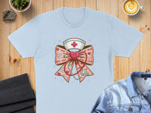 Load image into Gallery viewer, Light blue t-shirt with a pink ribbon, stethoscope, and nurse's hat graphic.
