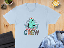 Load image into Gallery viewer, Light blue t-shirt with "Boo Boo Crew" ghost nurse graphic and medical tools.