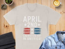 Load image into Gallery viewer, Cream t-shirt with "APRIL 2ND LIBERATION DAY IN AMERICA!" and US flag design.