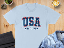 Load image into Gallery viewer, Light blue t-shirt with "USA EST. 1776" printed in red and blue.