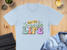Load image into Gallery viewer, Light blue t-shirt with "livin' the scrub life" text and colorful graphic.