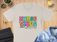 Load image into Gallery viewer, Nurse Vibes text with medical icons on a tan t-shirt.