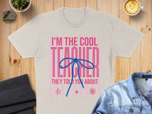 Load image into Gallery viewer, "I'm The Cool Teacher They Told You About" text on a light tan t-shirt with a blue bow.