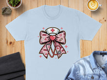 Load image into Gallery viewer, Light blue t-shirt with a pink nurse-themed bow featuring a stethoscope and crosses.